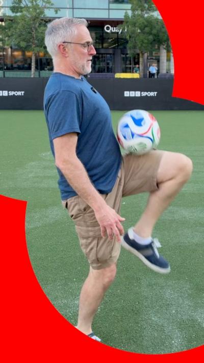 A man wearing shorts and a blue t-shirt keeps a football on his knee