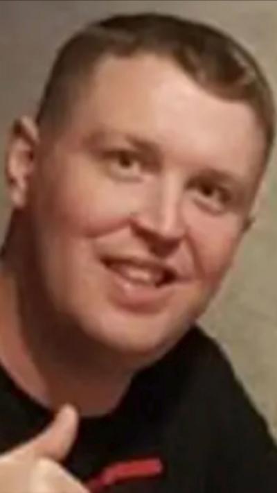 Robert Kincaid has short blond/brown hair. He is smiling and is wearing a black top. The back drop looks like wallpaper.