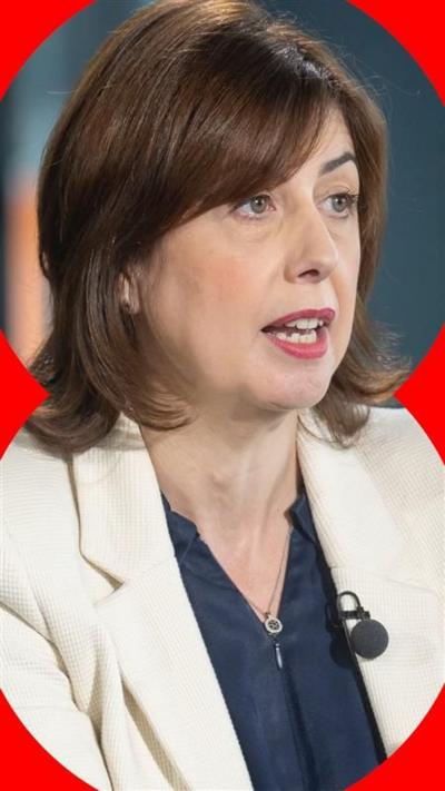 Labour MP Lucy Powell sat down being interviewed. She has shoulder length brown hair and wears a cream blazer