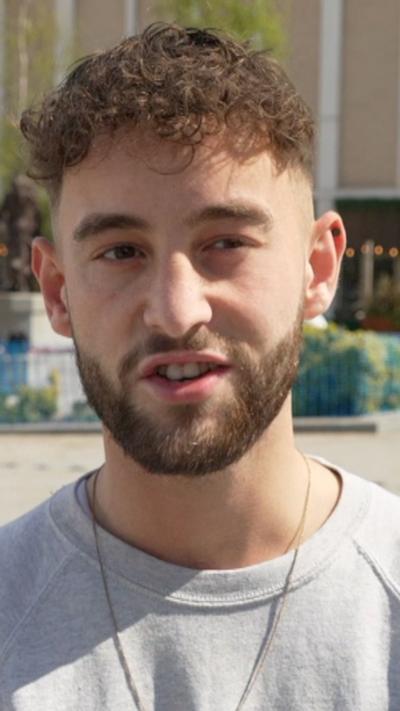 Man with brown hair and beard in a grey top and chain around his neck