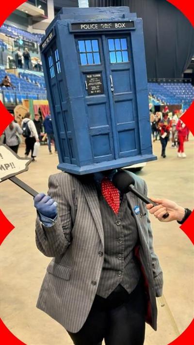 A person wearing a grey suit and a Doctor Who Tardis model over their head