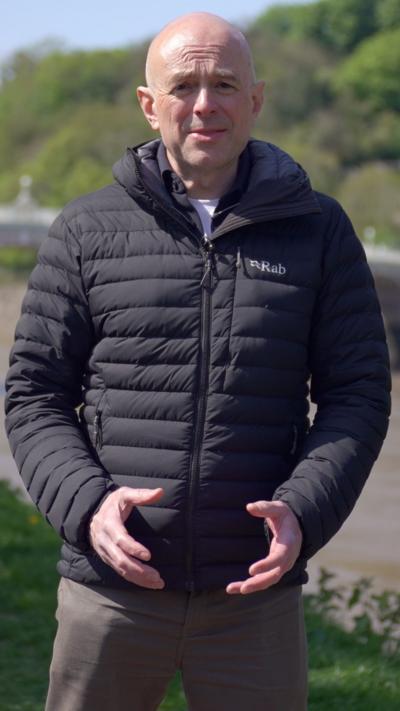 Gareth Lewis stood on a river bank in a black coat. He has a bald head