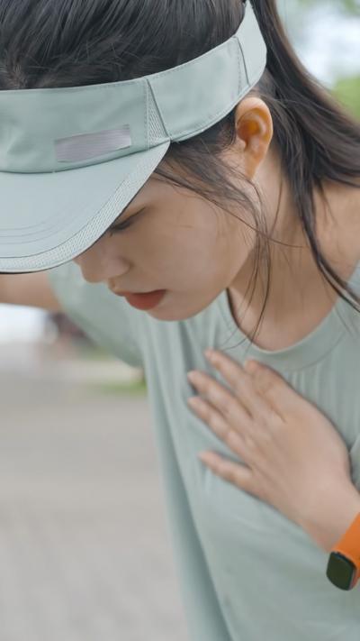 A woman with dark hair pulled back into a pony tail stands with her hand on her chest 