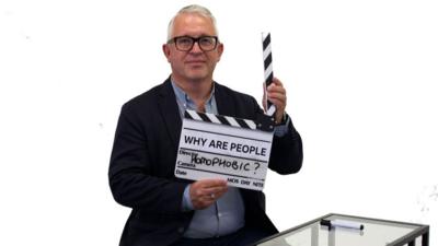 Man holds clapper-board with 'Why are people homophobic?" on it
