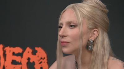 Singer Lady Gaga sits during an interview - she has long blonde hair and wears silver earrings