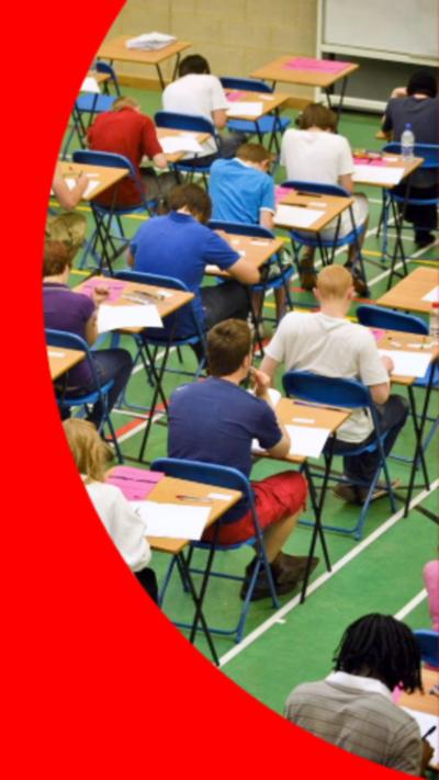Young people sat at square desks in an exam hall. They are wearing a variety of colours and the floor is bright green.