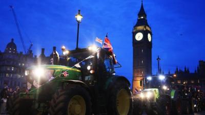 A tractor flying a union jack flag drives past Big Ben at night