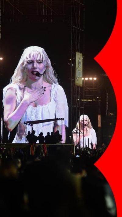 Lady Gaga in a white outfit, displayed on a big screen 