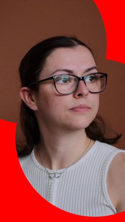 Lauryn McCready looks to her left. She wears black-rimmed glasses and a white vest top.