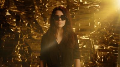 Young woman wearing sunglasses against a golden background 