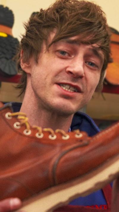 A man with medium length brown hair holding up a brown boot.