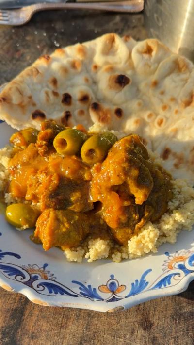 lamb tagine in a white bowl with couscous and olives on a wooden table outside