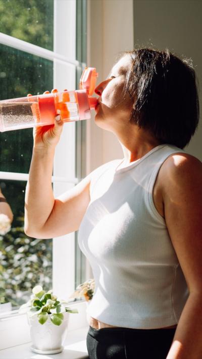 
Woman drinks water as she faces a window