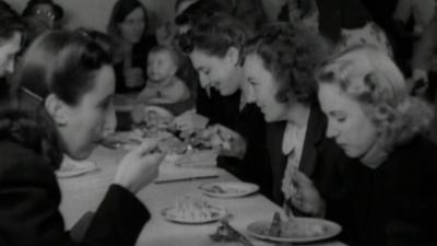 A group of women in the 1940s eat a meal at a long table
