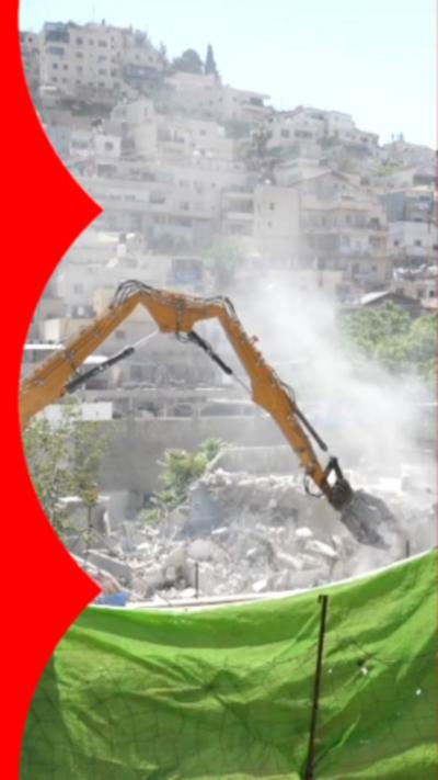 A yellow bulldozer engaging in the demolition of homes. It is behind a raised green net and behind it are other houses.