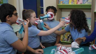 kids-in-a-school-pretending-to-brush-their-teeth-using-giant-toothbrushes-made-of-paper