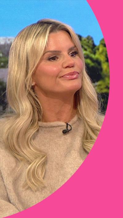 Kerry Katona sat on the BBC Breakfast red sofa. She has long blonde hair and wears a beige jumper