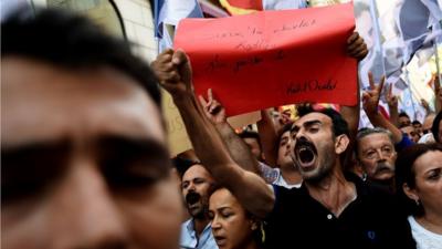 Protestors shout slogans and hold a placard reading "Goverment massacre in Suruc- killer goverment"