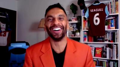 Bobby Seagull, wearing a red jacket, smiles at the camera. 