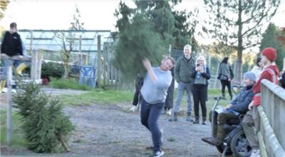 A man in a grey jumper and dark trousers throwing a Christmas tree over his shoulder.