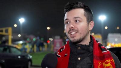 A Kettering Town fan, scarf draped around his neck, smiles as he talks about his side's win over Northampton Town.