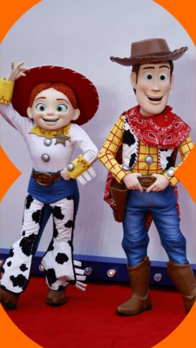 Toy Story characters Jessie, Woody and Buzz Lightyear stand in front of a sign for Toy Story 5