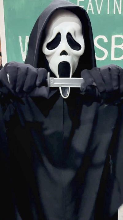 A person dressed in the costume from the Scream movies, wearing a black hooded cape and a white mask
