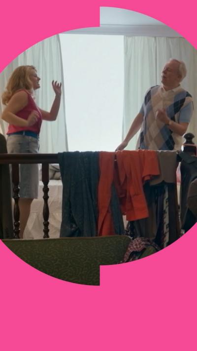 A woman and a man dance in a hotel room. Clothes are draped over a bannister 
