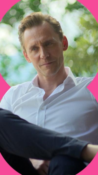 A man in a white shirt with the collar unbuttoned sits with his legs crossed