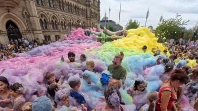 Multicoloured foam flows over adults and children in Centenary Square in Bradford