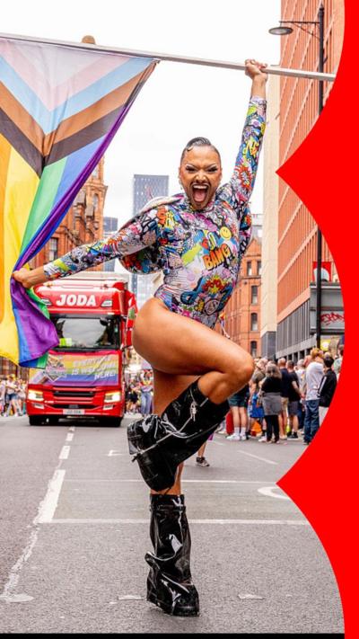 A person in a multicoloured body suit, holding a Pride flag, walks in the Manchester Pride parade on 23 August 2025