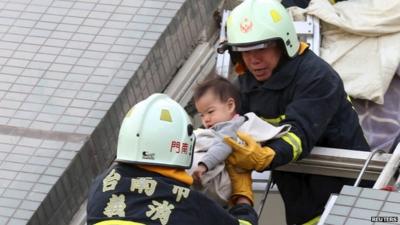 Rescue workers remove a baby from the site where a 17-storey apartment building collapsed after an earthquake hit Tainan,
