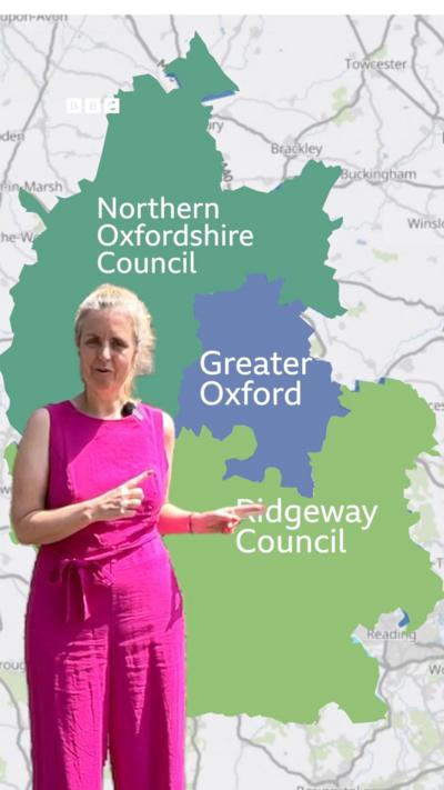 A woman in a pink outfit stands in front of a map of Oxfordshire.