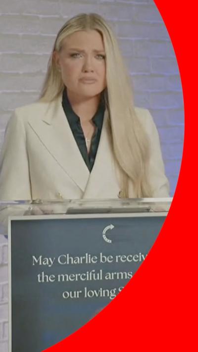 Erika Kirk with a tearful expression, stood at a podium. She is wearing a white suit.