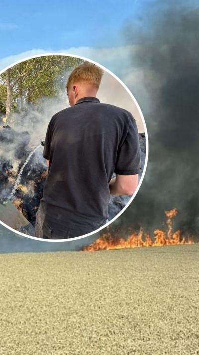 Farmers battle blaze on farmland. A ginger man holds equipment, firing water at a fire with thick black smoke.