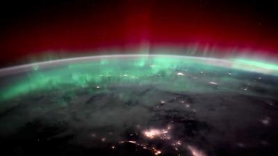 Northern Light as seen from space. The circular outline of Earth is lit up in a green and red glow.