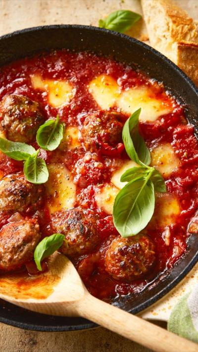 Top down view of a pan with fennel and chilli meatball bake. A wooden spoon is in the side of the dish.