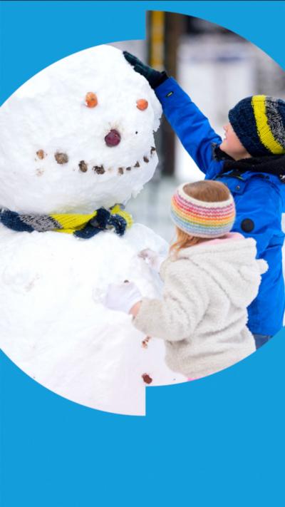 A young boy and girl, wearing blue and pink clothes, patting down snow on a snowman bigger than them