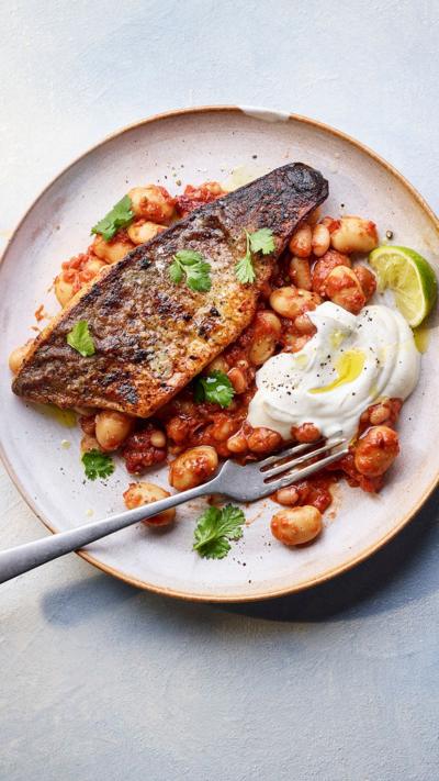 Top down view of a piece of fish on a bean stew. A fork sits on the plate