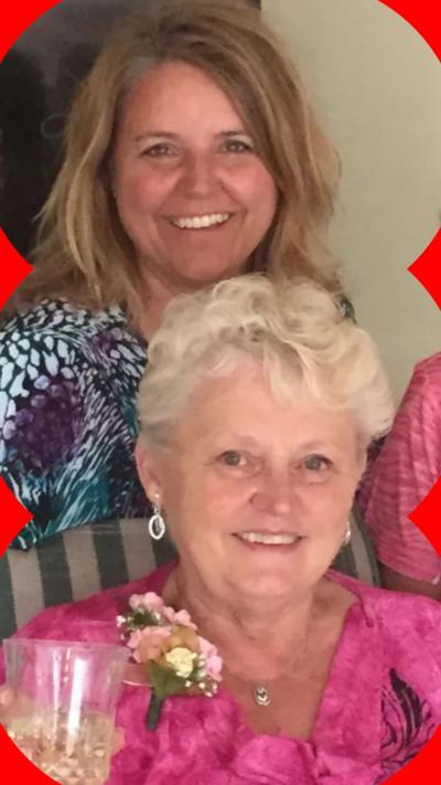Anita LeBrun, 82, wears a bright pink floral top and corsage, smiling as she holds up a glass of white wine as female members of her family stands behind her