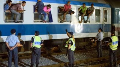 Police officers look at migrants sitting on the windows of a train at the railway station, near the Slovenian-Croatian border in Dobova, Brezice, on September 17, 2015.
