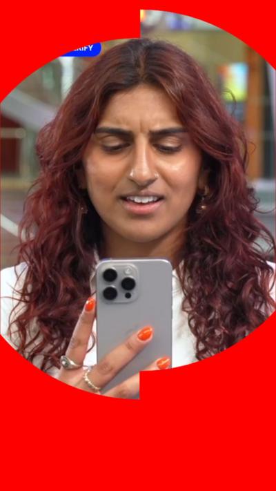 Woman with red hair holds a silver phone up to her face and looks confused