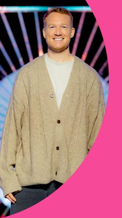 Greg Rutherford on the Drag Race UK set wearing an oversized cardigan