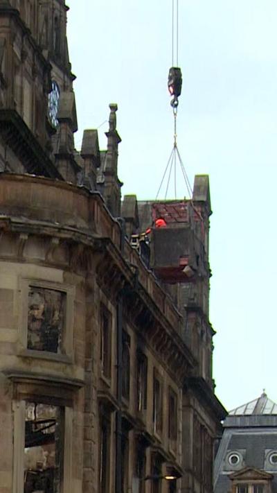Crane lowers debris container beside damaged historic building as demolition gets under way.