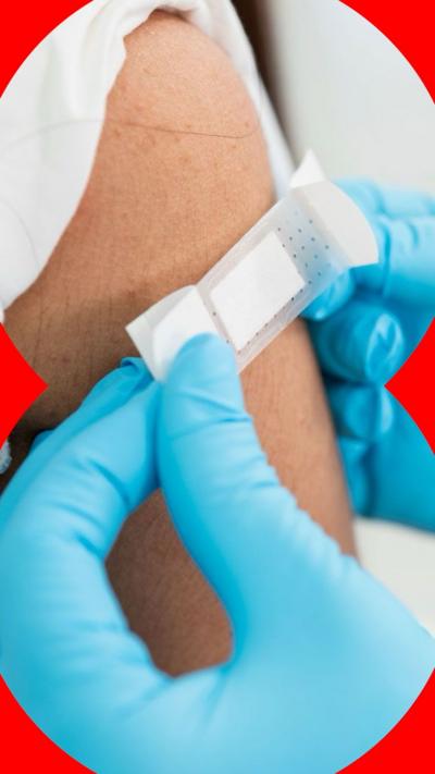A person wearing blue gloves places a plaster on an arm