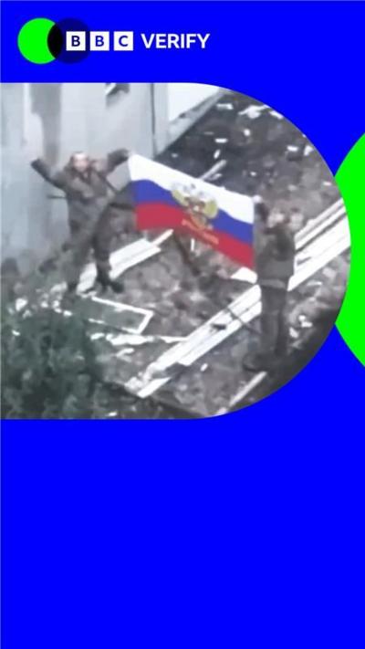 Two Russian soldiers hold a Russian flag aloft.