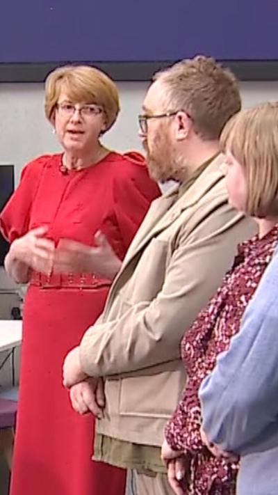 A woman in a red dress explains something to a fellow politician in a debate for the BBC.
