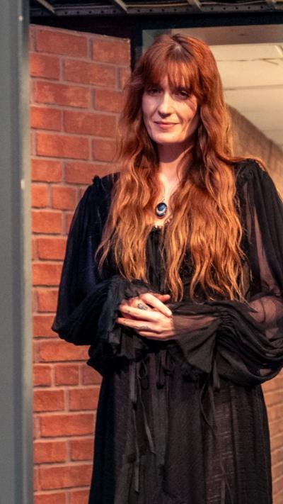 Florence Welch stands in a doorway, wearing a black dress. She has long wavy red hair