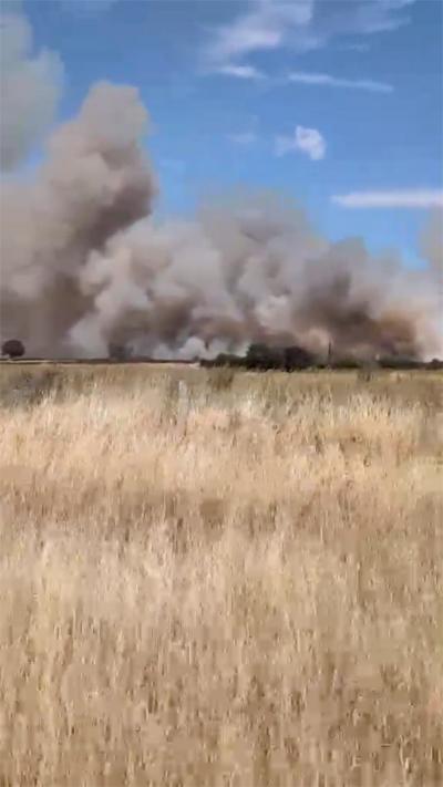 Smoke is rising from a field with hay into the blue sky.