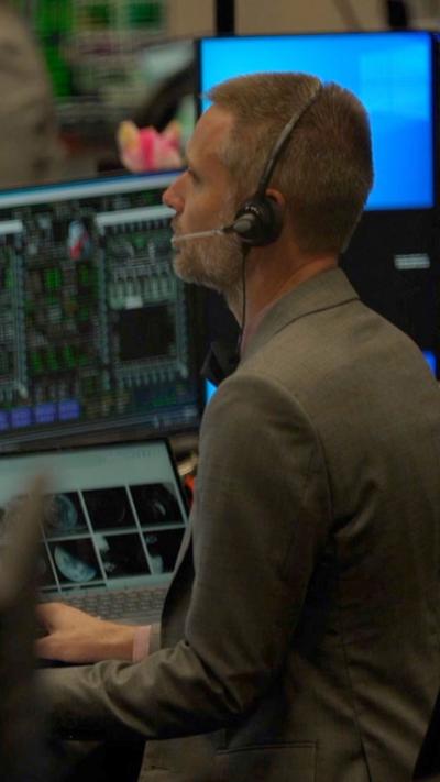 Mean wearing a headset looking at a bank of computers